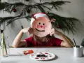 Dziecko w czapce Mikołaja tworzy świąteczne prace plastyczne w przedszkolu, trzymając przed twarzą własnoręcznie zrobioną maskę renifera.