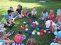 Dzieci siedzą na trawie, otoczone kolorowymi balonami. To wesołe zabawy z balonami dla dzieci na świeżym powietrzu.