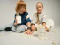 Dzieci siedzą na podłodze, jedząc popcorn z kubków. To idealny moment na wspólne oglądanie bajek, a kieszonkowe dla dziecka na przekąski zawsze się przyda.