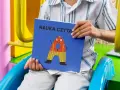 Chłopiec trzyma książkę "Nauka czytania dla dzieci 6 lat" z zabawną literką "A" na okładce.