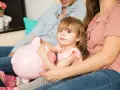 Mała dziewczynka z rodzicami przytulająca różową świnkę-skarbonkę. Zastanawiają się, ile kieszonkowego dla 10 latka.