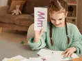 Dziewczynka uczy się literki "M". Na karcie widnieje duża i mała litera "m". To świetna zabawa z wyrazami na m dla dzieci.