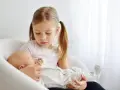 Starsza siostra delikatnie trzyma noworodka, ucząc się jak przygotować dziecko na rodzeństwo.