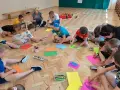 Wesołe zabawy w kole przedszkole. Dzieci siedzą na podłodze i rysują kolorowymi kredkami.
