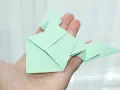 Zielona żaba z papieru, złożona techniką origami, spoczywa na dłoni.