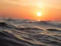 Piękne fale na morzu podczas zachodu słońca, jak z rysunku dla dzieci. Słońce maluje niebo na pomarańczowo.