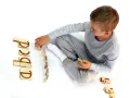 Chłopiec układa drewniane klocki z literami, ćwicząc czytanie klasa 1. Litery tworzą słowo "abcd".