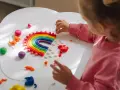 Dziecko tworzy tęczę z plasteliny, rozwiązując kreatywne wyzwania dla dzieci w domu. Kolorowa zabawa rozwija wyobraźnię.