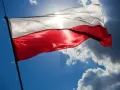 Biało-czerwona flaga powiewa na tle błękitnego nieba z chmurami. Wiatr rozwiewa ją, przypominając o pięknych cytatach o ojczyźnie.