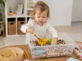 Roczne dziecko odkrywa świat przez zabawy sensoryczne, przesypując fasolki drewnianą łopatką.
