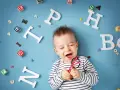 Uśmiechnięte dziecko z zabawkami-literkami wokół. Słyszy "mama" i cieszy się.