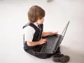 Elegancki chłopiec w garniturze odkrywa świat w internecie, siedząc na podłodze z laptopem.