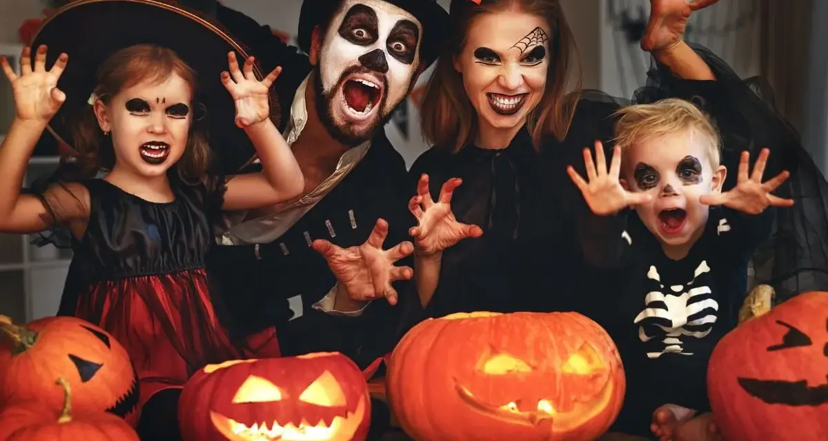Rodzina w strojach na Halloween, z dyniami i pajęczyną w tle. Idealne inspiracje na halloween karty pracy dla dzieci.