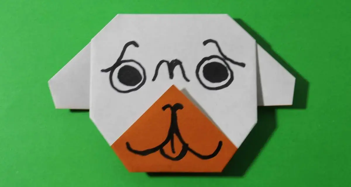 Urocza praca plastyczna: origami przedstawiające pyszczek psa z czarnymi oczami i pomarańczowym noskiem.