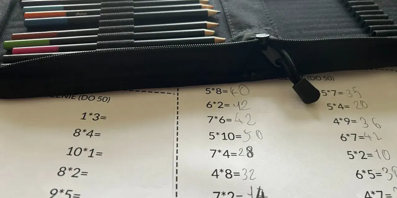 Karta pracy z tabliczką mnożenia do 100. Obok leżą kolorowe kredki w etui.