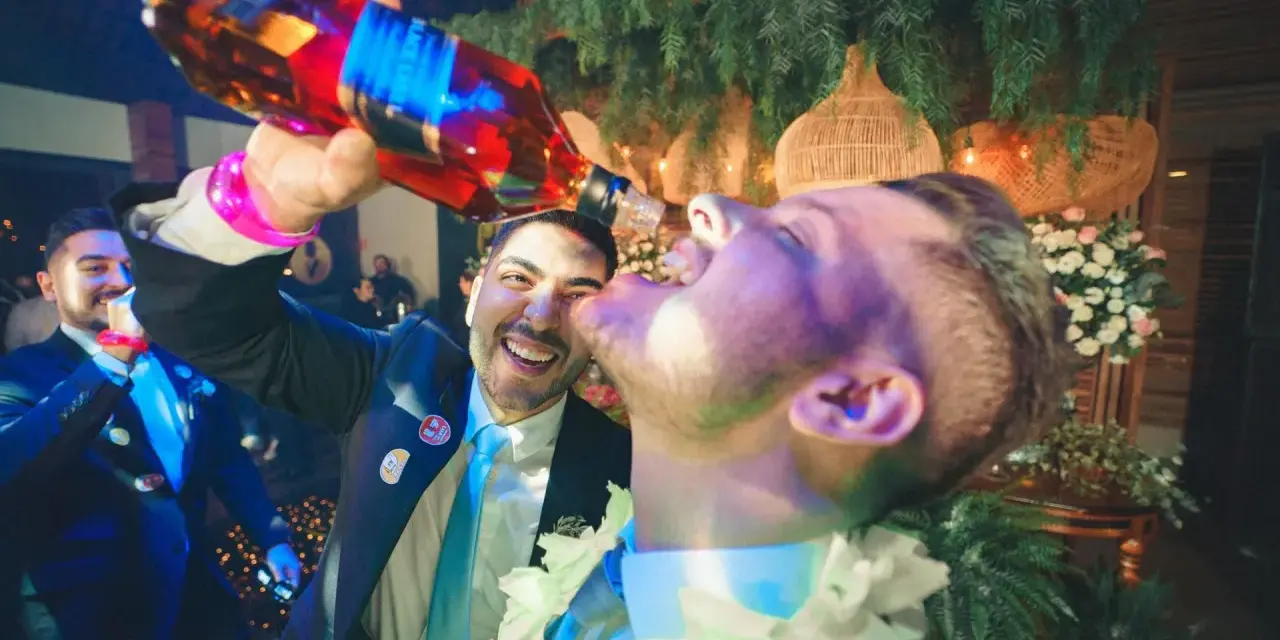 Szampańskie zabawy na imprezie! Mężczyzna nalewa alkohol prosto do ust przyjaciela, obaj uśmiechnięci i pełni radości.