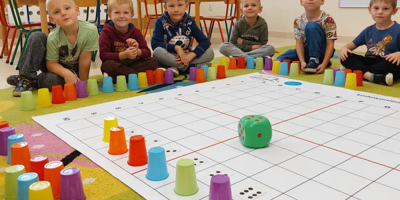 Dzieci uczą się kodowania dla przedszkolaków, bawiąc się kolorowymi kubeczkami i planszą z kostką.
