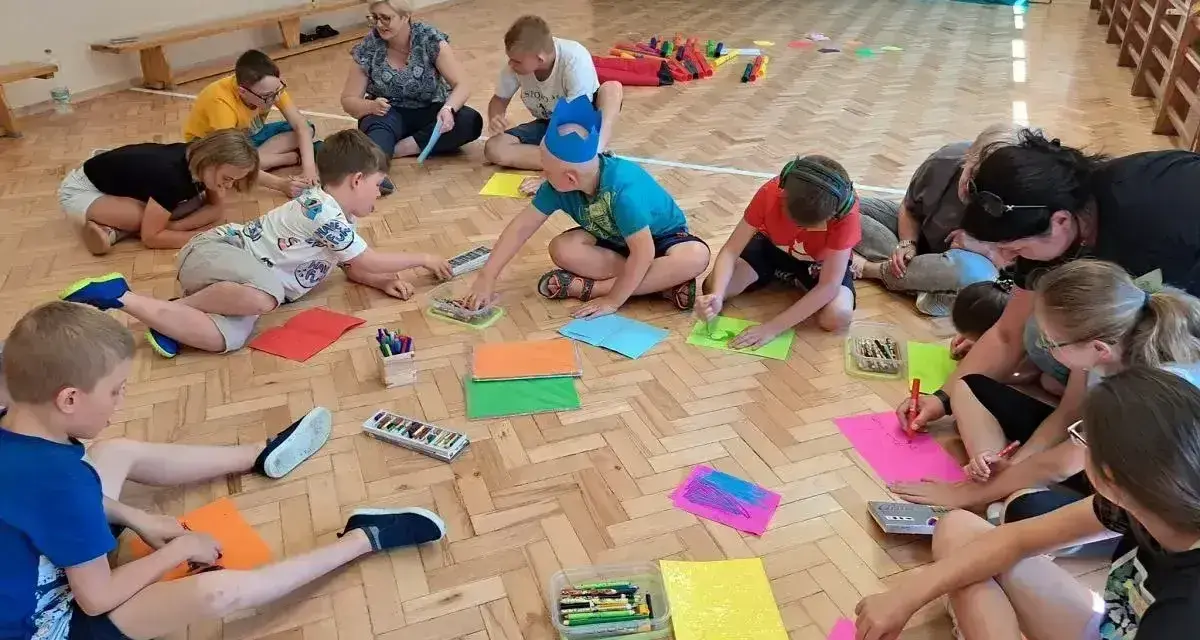 Wesołe zabawy w kole przedszkole. Dzieci siedzą na podłodze i rysują kolorowymi kredkami.