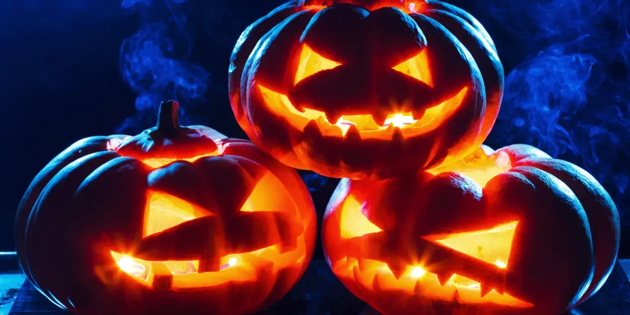 Trzy świecące **jack o lantern** z wyciętymi strasznymi minami, otoczone niebieską mgłą, tworzą mroczny, halloweenowy nastrój.