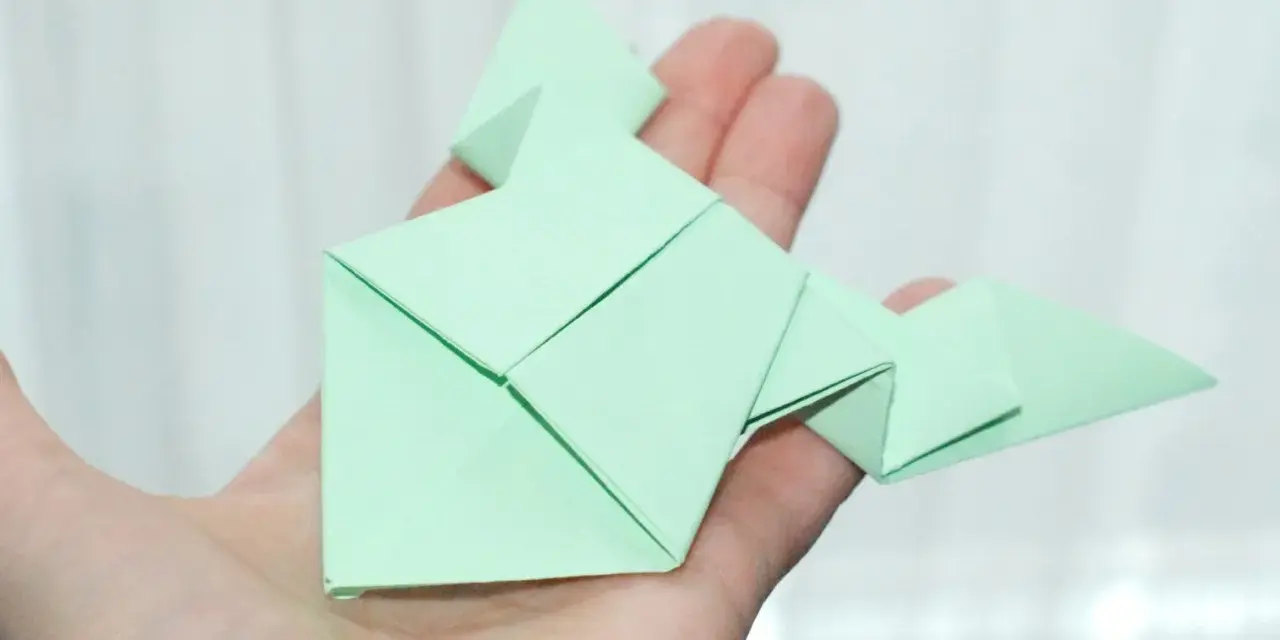 Zielona żaba z papieru, złożona techniką origami, spoczywa na dłoni.