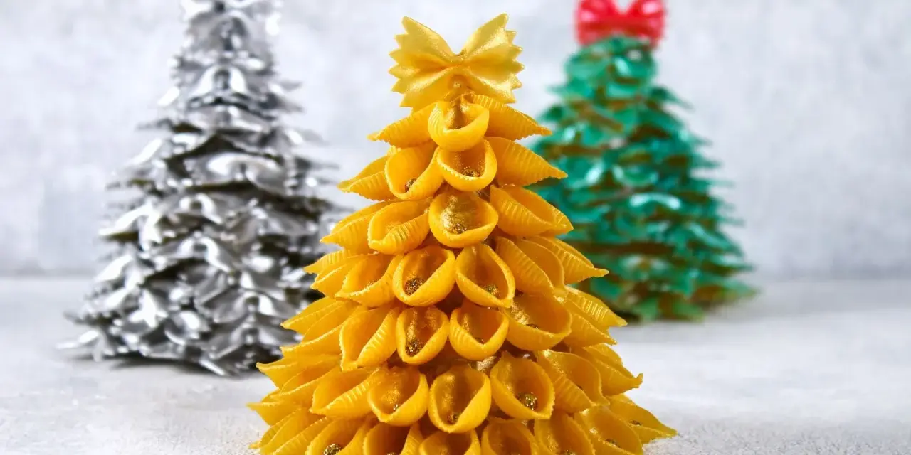 Choinka DIY dla dzieci z makaronu muszelki, ozdobiona złotym brokatem. W tle choinki z makaronu farfalle w kolorze srebrnym i zielonym.