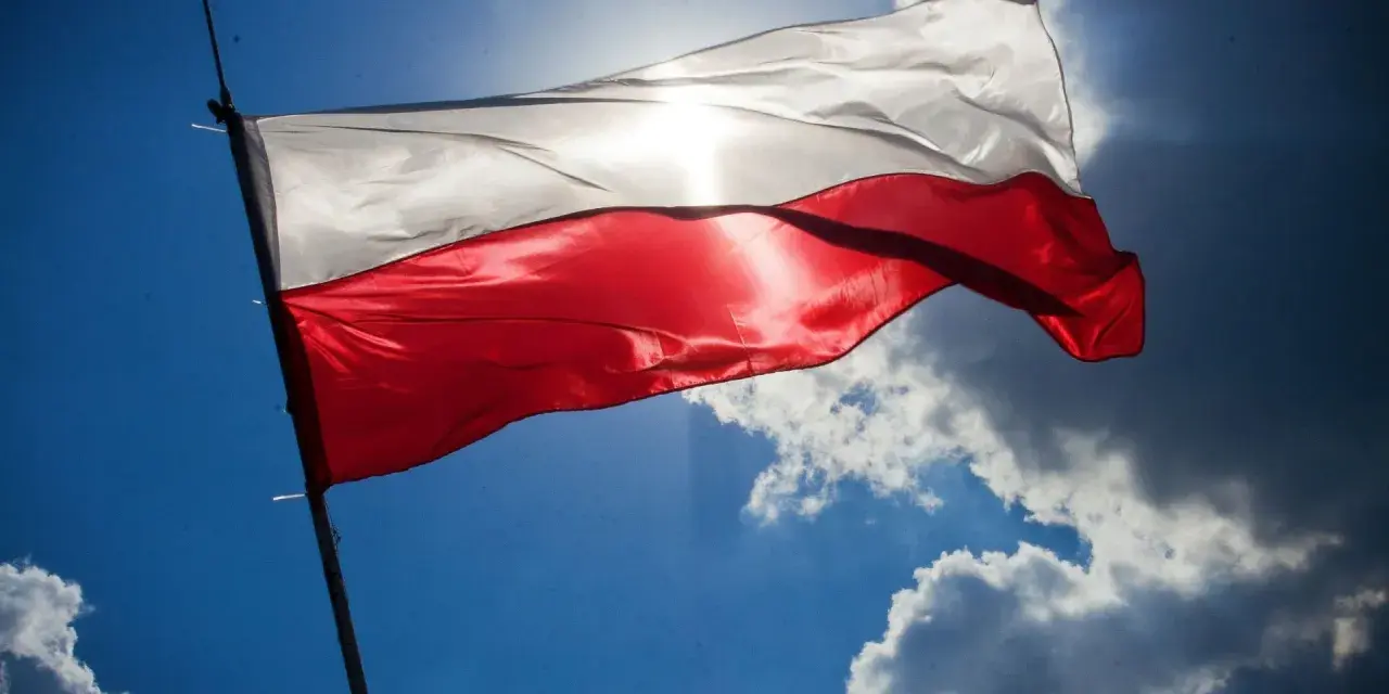 Biało-czerwona flaga powiewa na tle błękitnego nieba z chmurami. Wiatr rozwiewa ją, przypominając o pięknych cytatach o ojczyźnie.