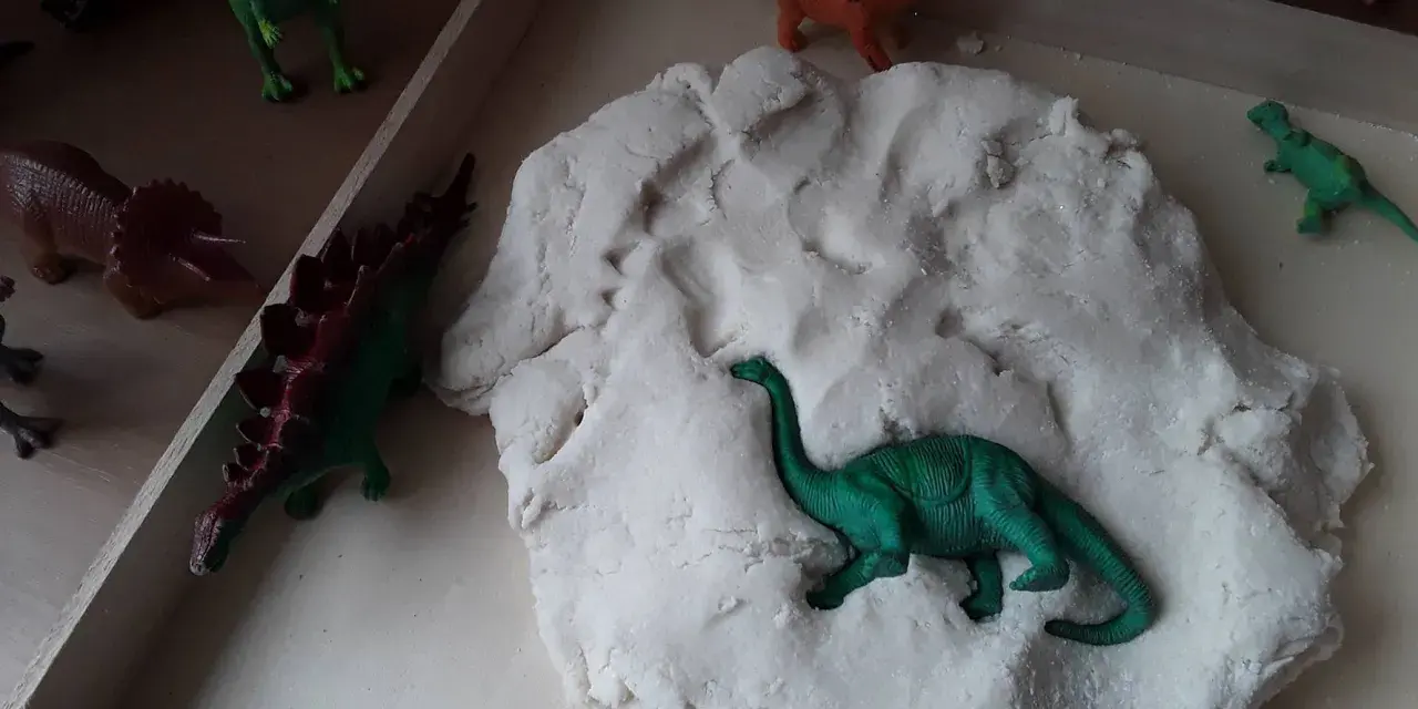 Zabawy z masą plastyczną i figurkami dinozaurów to świetne pomysły na dzień dinozaura. Dzieci mogą tworzyć prehistoryczne krajobrazy.