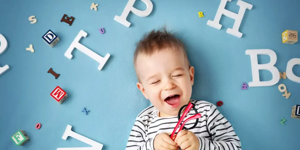 Uśmiechnięte dziecko z zabawkami-literkami wokół. Słyszy "mama" i cieszy się.