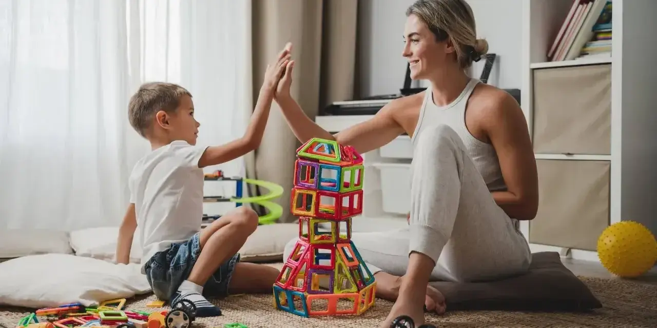 Mama i syn świętują sukces budowli z klocków magnetycznych. To świetne kreatywne zabawy dla 8 latka, rozwijające wyobraźnię i zdolności manualne.