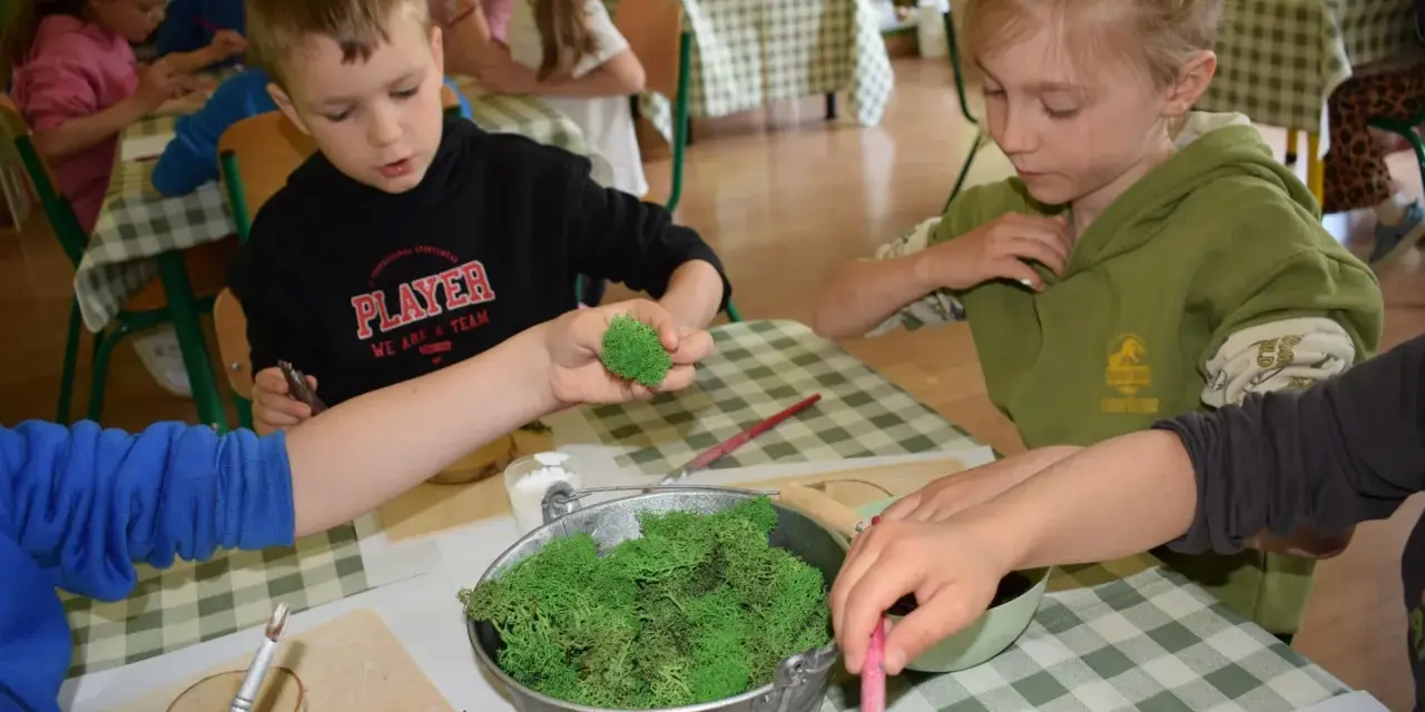 Dzieci tworzą leśne dekoracje na warsztatach. W wiaderku mech, a w rękach dzieci pędzelki i drewniane krążki. Świetne pomysły na warsztaty dla dzieci!