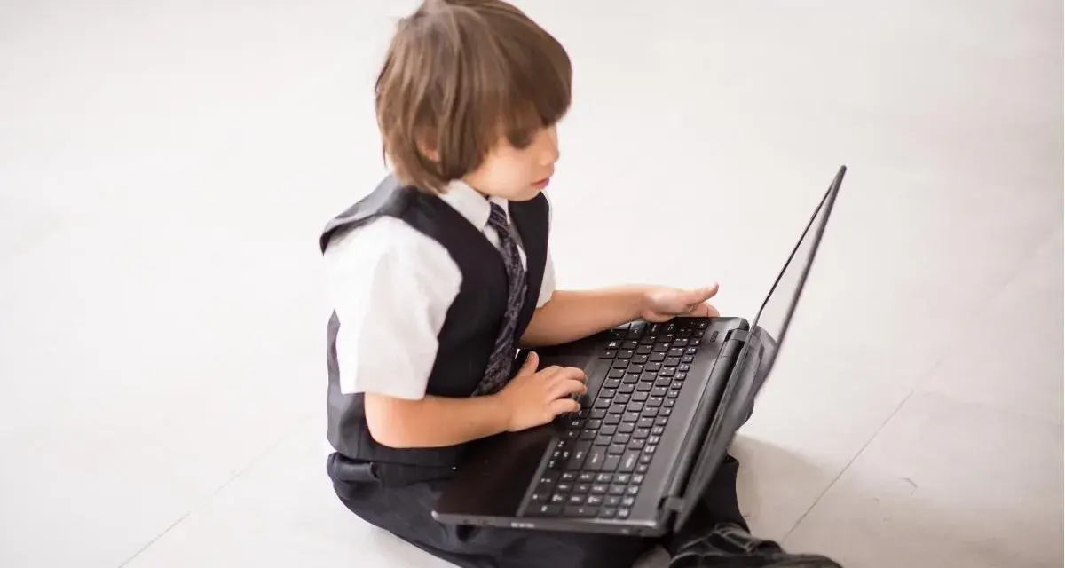 Elegancki chłopiec w garniturze odkrywa świat w internecie, siedząc na podłodze z laptopem.