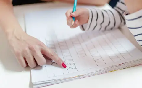 Dziecko ćwiczy pisanie, a dorosły pokazuje mu ćwiczenia grafomotoryczne klasa 1.