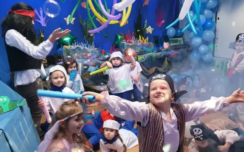 Dzieci w strojach piratów i wróżek bawią się na podwodnym balu karnawałowym. Balony i dekoracje tworzą atmosferę morskiej przygody.