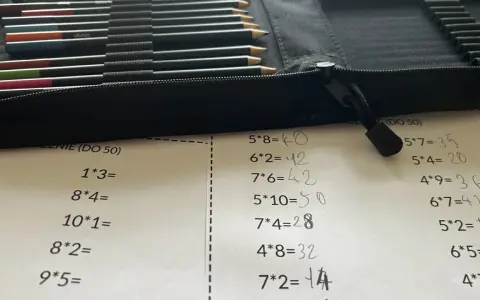 Karta pracy z tabliczką mnożenia do 100. Obok leżą kolorowe kredki w etui.
