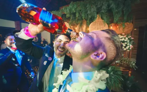 Szampańskie zabawy na imprezie! Mężczyzna nalewa alkohol prosto do ust przyjaciela, obaj uśmiechnięci i pełni radości.