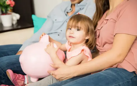 Mała dziewczynka z rodzicami przytulająca różową świnkę-skarbonkę. Zastanawiają się, ile kieszonkowego dla 10 latka.