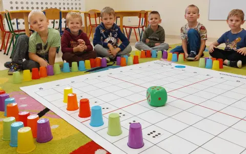 Dzieci uczą się kodowania dla przedszkolaków, bawiąc się kolorowymi kubeczkami i planszą z kostką.