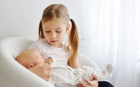 Starsza siostra delikatnie trzyma noworodka, ucząc się jak przygotować dziecko na rodzeństwo.