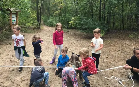 Dzieci biorą udział w leśnej grze terenowej, przeciągając linę.