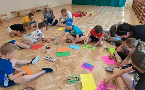 Wesołe zabawy w kole przedszkole. Dzieci siedzą na podłodze i rysują kolorowymi kredkami.