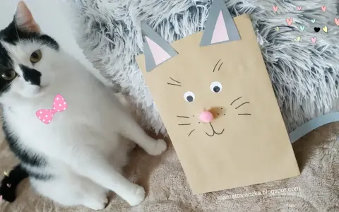 Urocza praca plastyczna kot z papierowej torby obok prawdziwego czarno-białego kota w różowej kokardce.