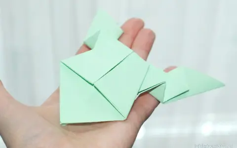Zielona żaba z papieru, złożona techniką origami, spoczywa na dłoni.
