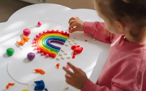 Dziecko tworzy tęczę z plasteliny, rozwiązując kreatywne wyzwania dla dzieci w domu. Kolorowa zabawa rozwija wyobraźnię.