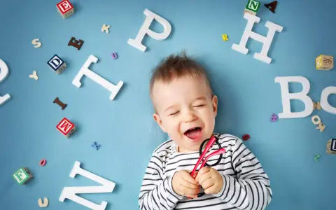 Uśmiechnięte dziecko z zabawkami-literkami wokół. Słyszy "mama" i cieszy się.