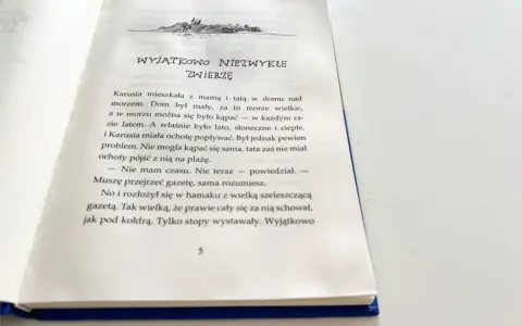 Piaskowy wilk bohaterowie: Karusia i tata nad morzem. Tata czyta gazetę, a Karusia chce popływać.