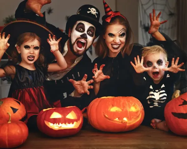 Rodzina w strojach na Halloween, z dyniami i pajęczyną w tle. Idealne inspiracje na halloween karty pracy dla dzieci.
