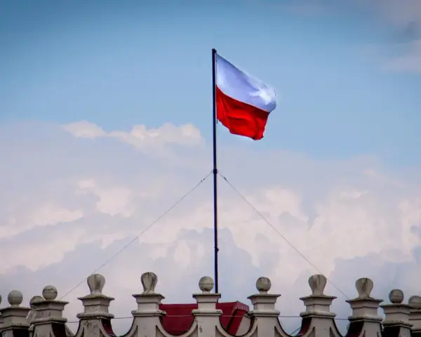 Biało-czerwona flaga powiewa na maszcie nad zabytkowym budynkiem. Wiatr rozwiewa ją, jakby niosła słowa o Polsce.
