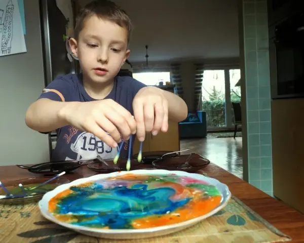 Chłopiec tworzy kolorowe wzory na mleku, dotykając jego powierzchni patyczkami higienicznymi. To fascynujące malowanie na mleku!