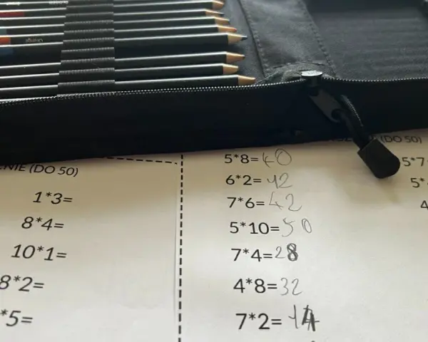 Karta pracy z tabliczką mnożenia do 100. Obok leżą kolorowe kredki w etui.