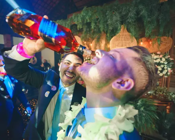 Szampańskie zabawy na imprezie! Mężczyzna nalewa alkohol prosto do ust przyjaciela, obaj uśmiechnięci i pełni radości.